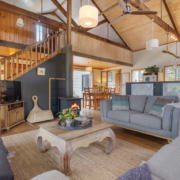Main Living Area: An open plan living room with wood heater, timber beams, ceiling fan and comfy sofas centered around a coffee table.