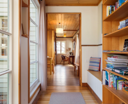 Mandala Bruny Island Hallway View: A perspective looking over office corner, a bright hallway with polished wood floors and a bookshelf on the right.