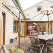 Outdoor Deck Entrance: A view looking out from the house onto a wooden deck area with an outdoor dining set and a large umbrella.