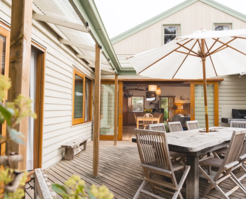 Outdoor Deck Entrance: A view looking out from the house onto a wooden deck area with an outdoor dining set and a large umbrella.